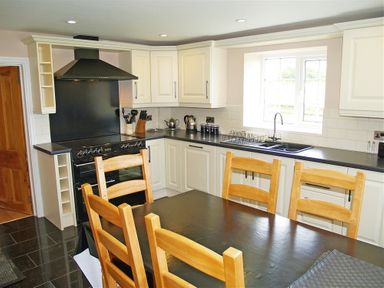 A kitchen with wooden chairs around a black table and white cabinets at Sarnau in Efailwen Carmarthenshire