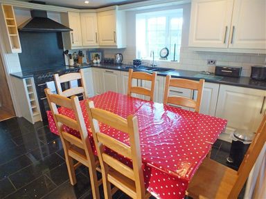 A kitchen with a black stove white cabinets a red polka dot tablecloth on a wooden table and wooden chairs at Sarnau in Efailwen Carmarthenshire