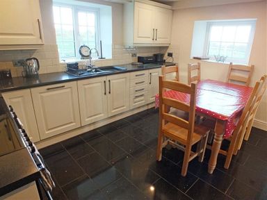 A kitchen with white cabinets black countertops wooden dining table with red polka dot tablecloth and wooden chairs at Sarnau in Efailwen Carmarthenshire