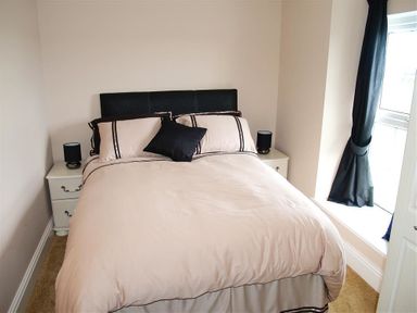 A bedroom with a double bed with beige bedding and black pillow beside two white bedside tables with black lamps at Sarnau in Efailwen Carmarthenshire