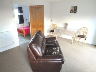 A room with a brown leather sofa cushions a small table with a polka dot tablecloth and two wooden chairs a doorway showing a bedroom with a red bed Sarnau Efailwen Carmarthenshire