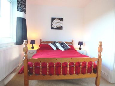 A bedroom with a wooden bed with a red bedspread two bedside tables with lamps and a window with curtains at Sarnau in Efailwen Carmarthenshire