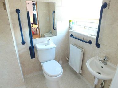 A bathroom with a toilet a sink a mirror and grab bars next to window and toilet at Sarnau in Efailwen Carmarthenshire