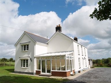 A white two-story house with a glass conservatory surrounded by grass and gravel driveway at Sarnau in Efailwen Carmarthenshire