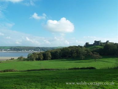 A green field with trees and a castle on a hill with a river and houses in the background at Sarnau in Efailwen Carmarthenshire