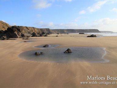 A sandy beach with scattered rocks and cliffs in the background at Marloes Beach