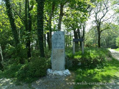A stone monument surrounded by trees and greenery beside a small signpost at Sarnau in Efailwen Carmarthenshire
