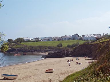 A sandy beach with small boats and people near cliffs and houses in the background at Beach Retreat in Aberporth