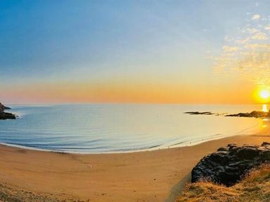 A beach with calm water and a rocky shore at sunset at Beach Retreat in Aberporth
