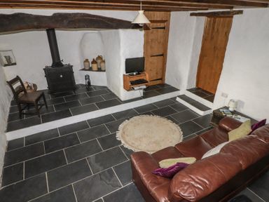 A living room with a leather sofa a rug a wood burning stove and a small television at Panteurig Cottage in Strumble Head Goodwick Pembrokeshire