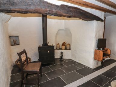 A corner with a wood stove black chair ceramic jugs and a small television on a wooden shelf at Panteurig Cottage in Strumble Head Goodwick Pembrokeshire