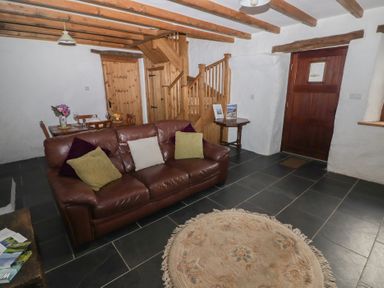 A living room with a leather sofa and pillows a round rug visible wooden stairs and a dining table at Panteurig Cottage in Strumble Head Goodwick Pembrokeshire