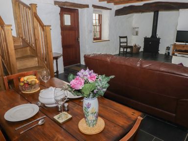 A dining table with plates glasses a vase with flowers and fruit bowl near a leather sofa and wood stove in a cottage living room at Panteurig Cottage Strumble Head Goodwick Pembrokeshire