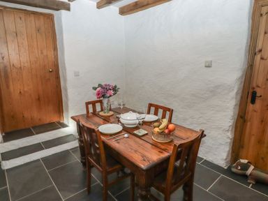 A dining area with a wooden table set with plates glassware and fruit bowl with two wooden doors in a room at Panteurig Cottage in Strumble Head Goodwick Pembrokeshire