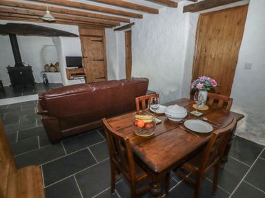 A dining table with plates and fruit bowl next to a brown leather sofa and fireplace at Panteurig Cottage in Strumble Head Goodwick Pembrokeshire