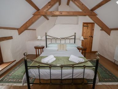 A bedroom with a metal bed frame two bedside tables with lamps wooden beams and a door at Panteurig Cottage in Strumble Head Goodwick Pembrokeshire