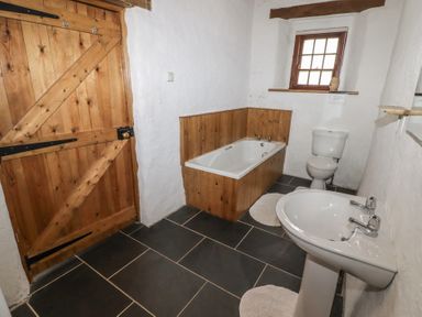 A bathroom with a wooden door a bathtub with wooden paneling a toilet a sink and a small window at Panteurig Cottage in Strumble Head Goodwick Pembrokeshire