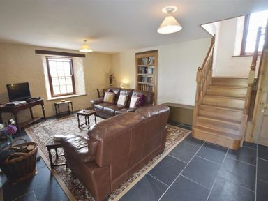A living room with brown leather sofas a wooden staircase a bookshelf a television and a patterned rug at Panteurig Farmhouse in Strumble Head Goodwick Pembrokeshire