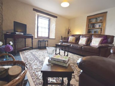 A living room with leather sofas a bookshelf a television on a wooden table and a patterned rug at Panteurig Farmhouse in Strumble Head Goodwick Pembrokeshire