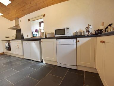 A kitchen with white cabinets black countertops a microwave dishwasher stove and window at Panteurig Farmhouse in Strumble Head Goodwick Pembrokeshire
