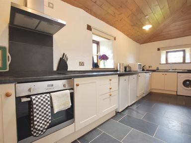 A kitchen with cabinets oven towels fridge microwave washing machine and flowers on the windowsill at Panteurig Farmhouse in Strumble Head Goodwick Pembrokeshire