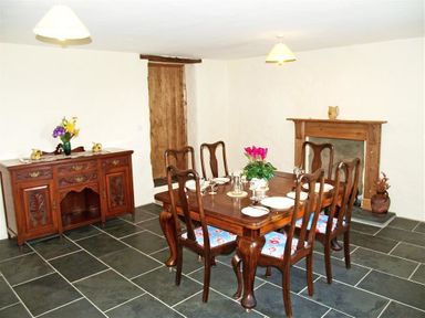 A dining room with a wooden table and six chairs set with plates glasses and silverware at Panteurig Farmhouse Strumble Head Goodwick Pembrokeshire