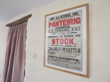 A framed poster with text about a clearout sale on a white wall next to a doorway with a curtain at Panteurig Farmhouse Strumble Head Goodwick Pembrokeshire