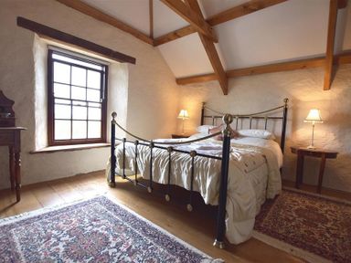 A bedroom with a metal bed frame two rugs wooden beams and two bedside tables with lamps at Panteurig Farmhouse in Strumble Head Goodwick Pembrokeshire
