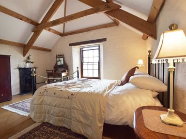 A bedroom with a bed a wooden dressing table a wardrobe and exposed wooden beams at Panteurig Farmhouse in Strumble Head Goodwick Pembrokeshire