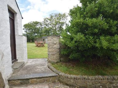An outdoor area with stone steps leading to a grassy garden with wooden table and chairs and trees nearby at Panteurig Farmhouse Strumble Head Goodwick Pembrokeshire