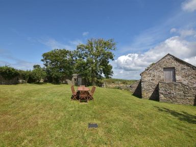 An outdoor area with wooden table and chairs on grass near stone buildings at Panteurig Farmhouse in Strumble Head Goodwick Pembrokeshire