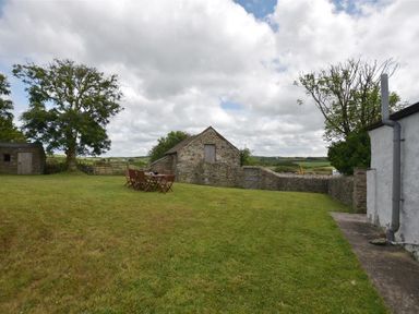 A grassy yard with a stone outbuilding a tree and outdoor table and chairs at Panteurig Farmhouse in Strumble Head Goodwick Pembrokeshire