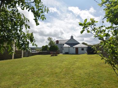A grassy yard with a table and chairs in front of a white farmhouse at Panteurig Farmhouse Strumble Head Goodwick Pembrokeshire