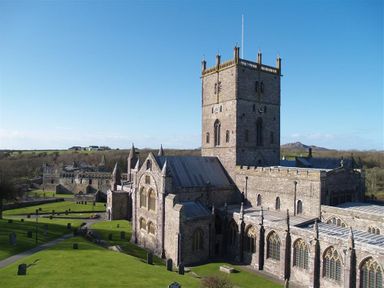 A stone cathedral with a large square tower and arched windows surrounded by grass and pathways