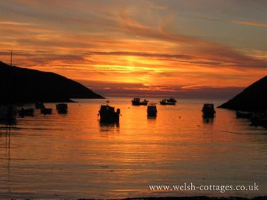 A sunset over a bay with boats on the water and hills on either side at Panteurig Farmhouse Strumble Head Goodwick Pembrokeshire