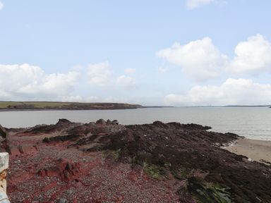 A rocky shoreline with water and distant land under a partly cloudy sky at Blackrock Boathouse in Dale Pembrokeshire