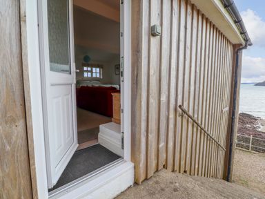 An open white door leading into a room with a red couch and a window overlooking the sea at Blackrock Boathouse in Dale Pembrokeshire