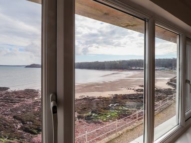 A coastal view of a rocky beach and shoreline through a large window at Blackrock Boathouse in Dale Pembrokeshire