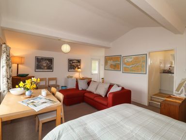 A living area with a red sofa, wooden dining table with chairs, a bed, framed maps and pictures on walls at Blackrock Boathouse in Dale Pembrokeshire