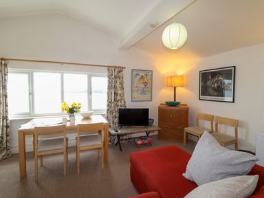 A living room with a red sofa chairs dining table and a television at Blackrock Boathouse in Dale Pembrokeshire