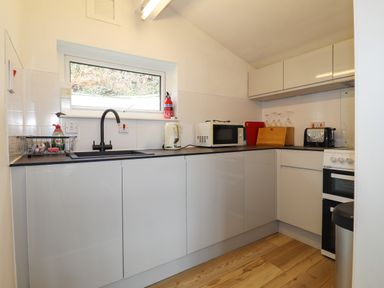 A kitchen with a sink microwave kettle toaster stove and cupboards at Blackrock Boathouse in Dale Pembrokeshire