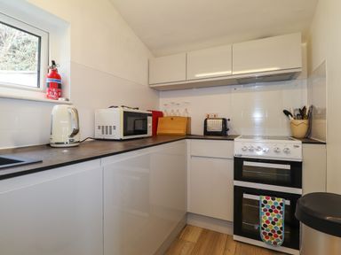 A kitchen with a white kettle microwave toaster oven cabinets and a fire extinguisher at Blackrock Boathouse in Dale Pembrokeshire