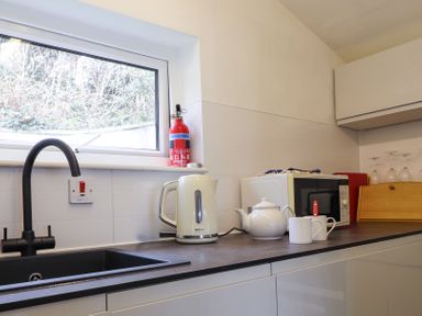 A kitchen countertop with a black sink faucet white kettle teapot two mugs microwave fire extinguisher and wine glasses at Blackrock Boathouse in Dale Pembrokeshire