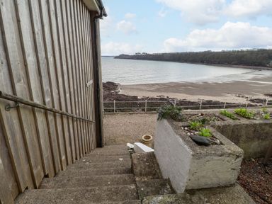 Stone steps next to a wooden building leading down to a beach with a gravel path and a low concrete planter at Blackrock Boathouse in Dale Pembrokeshire