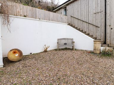 An outdoor area with gravel ground a wooden bench against a white wall stairs with wooden paneling and a large round buoy Blackrock Boathouse Dale Pembrokeshire