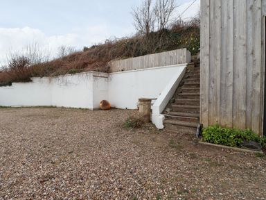 An outdoor area with gravel ground, concrete stairs, a white retaining wall, wooden fencing, and some plants at Blackrock Boathouse in Dale Pembrokeshire