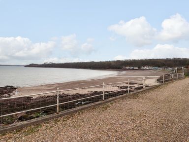 A view of a sandy beach and a rocky shoreline with a gravel path and metal railing in the foreground at Blackrock Boathouse in Dale Pembrokeshire