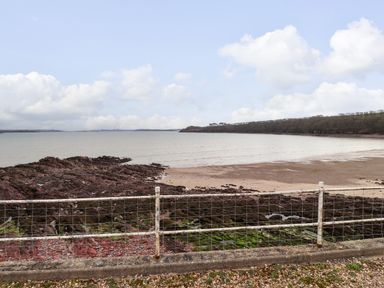 A view of a rocky beach and water with a wire fence in the foreground at Blackrock Boathouse in Dale Pembrokeshire