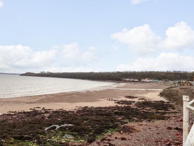 A wide sandy beach with rocky areas along the shore and houses in the distance at Blackrock Boathouse in Dale Pembrokeshire