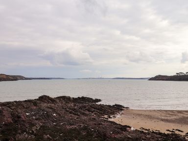 A rocky shoreline next to a sandy beach with water and distant land on the horizon at Blackrock Boathouse in Dale Pembrokeshire